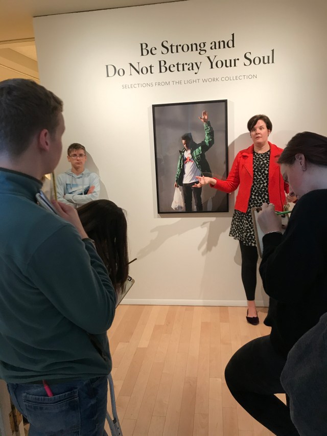 Woman standing in front of art photograph as students look on