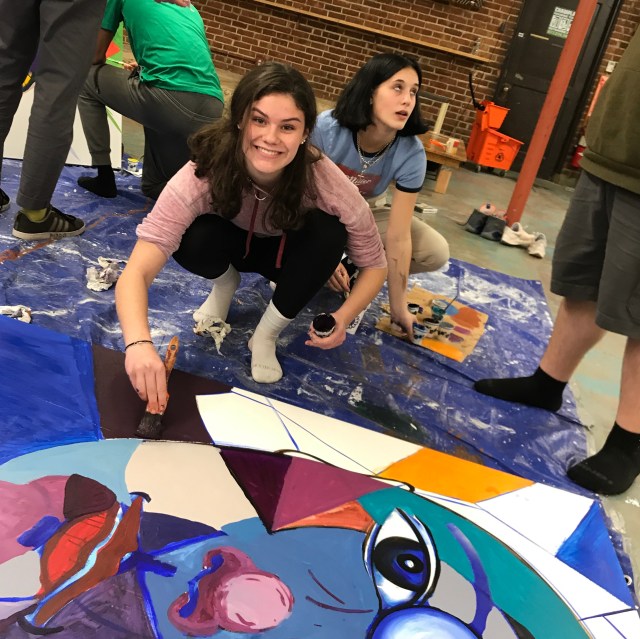 Student painting large canvas with face on it