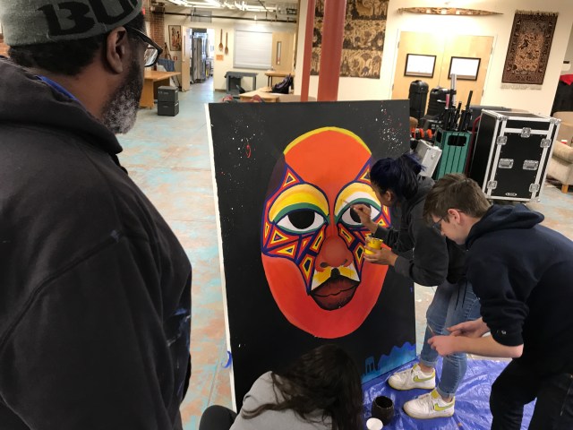 Students paint canvas as mentor artist looks on