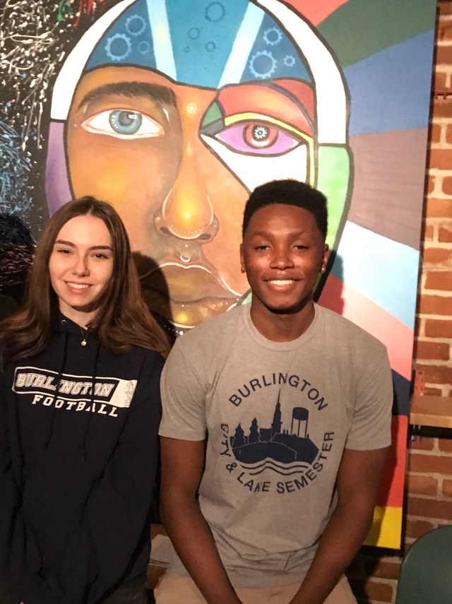 Two students in front of painting of face